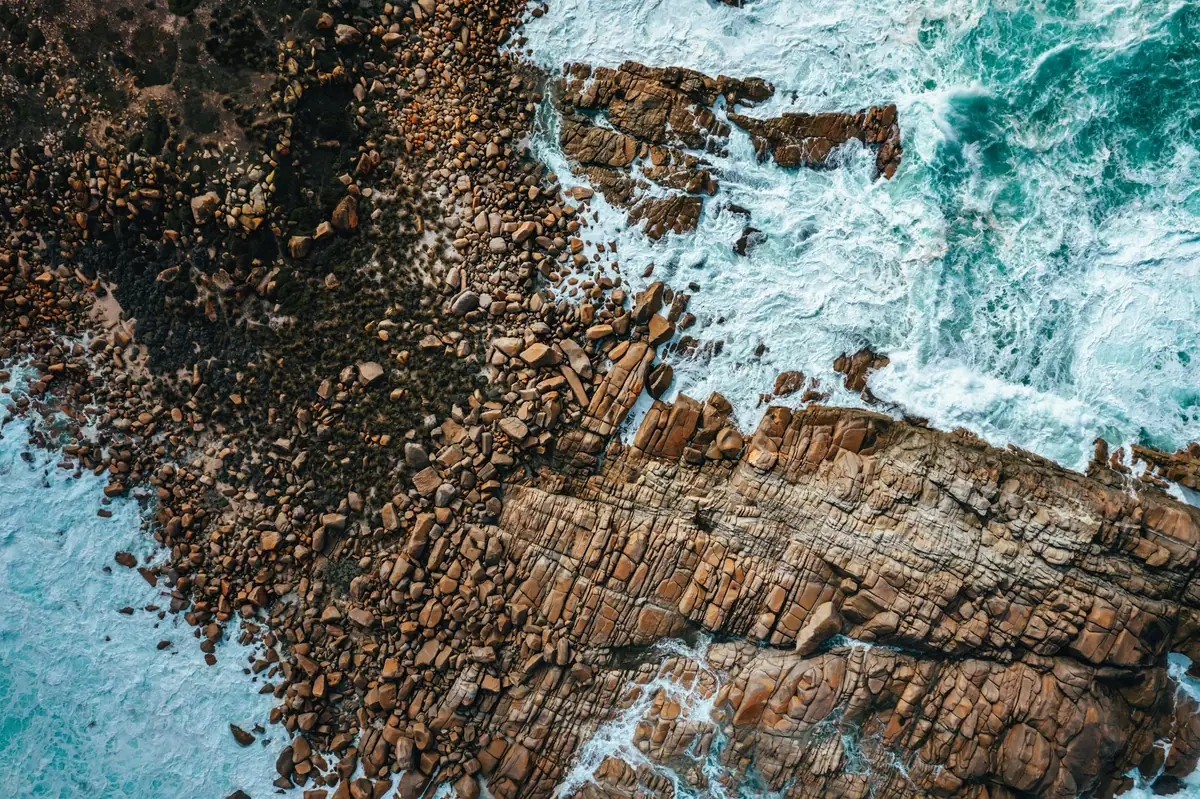 Top-down aerial of layered rock ledges and white surf along Kangaroo Island's rugged coast
